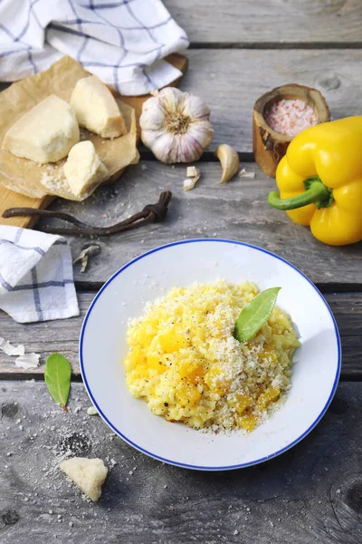 Italian food. Plate of yellow bell pepper risotto and grated parmesan cheese on wooden background. Top view