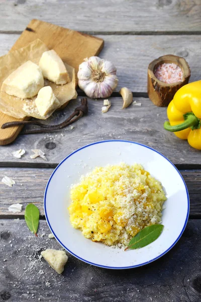 Italian food. Plate of yellow bell pepper risotto and grated parmesan cheese on wooden background. Top view