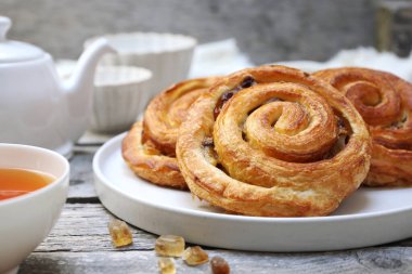 Fransız usulü üzümlü çörek, çaydanlık ve çay. Gri ahşap arka planda tatlı kahvaltı için.