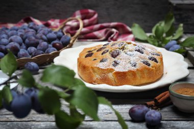 Tarçınlı ev yapımı erik turtası, pudra şekeri sosu ve ahşap zemin üzerinde taze mavi erikler. Seçici odaklan