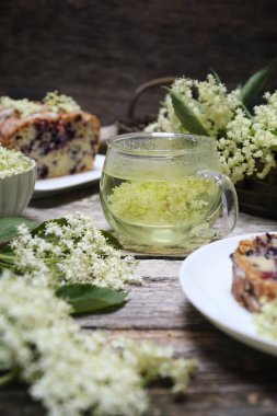 Mürver çiçeği çayı. Bir fincan sağlıklı bitkisel eritilmiş mürver çiçeği ve ahşap arka planda elderberry keki.