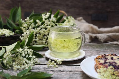 Mürver çiçeği çayı. Bir fincan sağlıklı bitkisel eritilmiş mürver çiçeği ve ahşap arka planda elderberry keki.