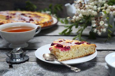İtalyan tatlısı. Ahududu ekşi kremalı pasta, bir fincan çay ve çiçek açan beyaz akasya.