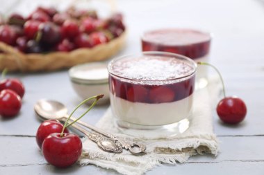 İki bardakta vişneli panna cotta, hindistan cevizi gevreği sosu ve açık yüzeyde taze kiraz. Seçici odaklan
