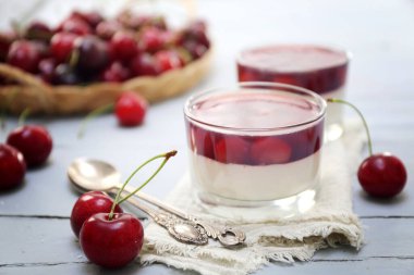 İki bardakta vişneli panna cotta ve ışık yüzeyinde taze kiraz. Seçici odaklan