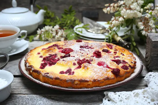 İtalyan tatlısı. Ahududu ekşi kremalı pasta, bir fincan çay ve çiçek açan beyaz akasya.