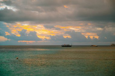 Maldivler 'de altın gün batımında okyanusta yüzen tekneler. Dramatik bulutlar ve canlı renkler barışçıl bir deniz manzarası yaratır.