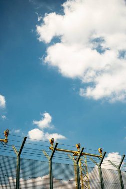 Havaalanı güvenlik çiti yeşil tel örgü ve sarı metal kule yapısının arkasında pist ışıkları var..