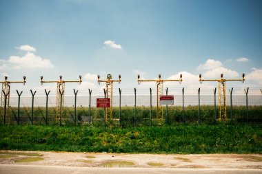 Havaalanı çevre çitlerinde tehlike işareti var. Işıklandırma yapısı ve jet patlaması ve İtalyan ve İngilizce uçak aktiviteleri uyarısı var.
