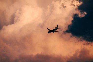 Dramatik alacakaranlık bulutları arasında uçan uçağın silueti. Gün batımında, fırtınanın kenarlarında, altın-pembe gökyüzü. Kontrastla ve hareketle dolu havacılık sahnesi