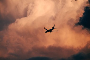 Dramatik alacakaranlık bulutları arasında uçan uçağın silueti. Gün batımında, fırtınanın kenarlarında, altın-pembe gökyüzü. Kontrastla ve hareketle dolu havacılık sahnesi
