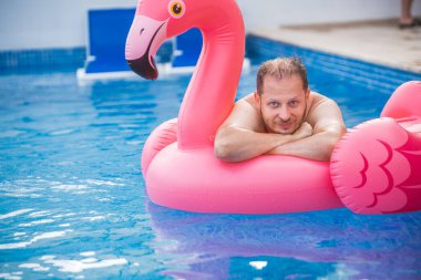Flamingodaki neşeli adam havuzda eğleniyor. Havuz flamingosunda rahatlayan mutlu bir adam. Seyahat yaz tatili kavramı.