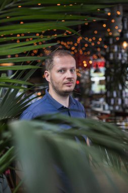 Genç, çekici ve yakışıklı bir adam tropikal bir palmiye ağacında arka planda bokeh ışıkları var.. 