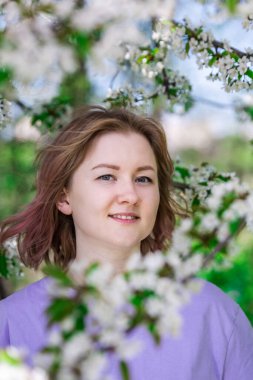 Bahar aylarında mor tişörtlü bir kadın. Elma bahçesinde beyaz çiçekli yumuşak bir fotoğraf..