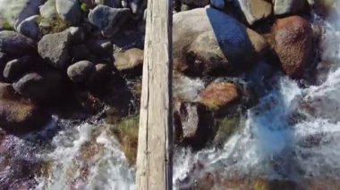 Kırgızistan 'da engebeli bir nehirde tahta köprüden geçen bir adam..