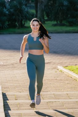 Sportif ve güler yüzlü genç bayan spor giyim koçu parkta koşuyor. Spor açık hava konsepti.