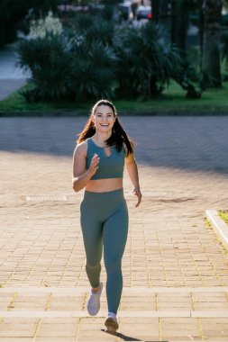 Sportif ve güler yüzlü genç bayan spor giyim koçu parkta koşuyor. Spor açık hava konsepti.