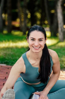 Sportif ve güler yüzlü genç bayan spor giyim koçu kırmızı koşu pistinde esneme egzersizleri yapıyor. Spor açık hava konsepti.