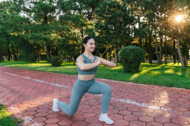 Sportif ve güler yüzlü genç bayan spor giyim koçu kırmızı koşu pistinde hamleler yapıyor. Spor açık hava konsepti.