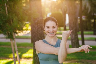 Sportif ve güler yüzlü genç bayan spor giyim koçu yeşil yaz parkında fiziksel esneme egzersizleri yapıyor. Spor açık hava konsepti.