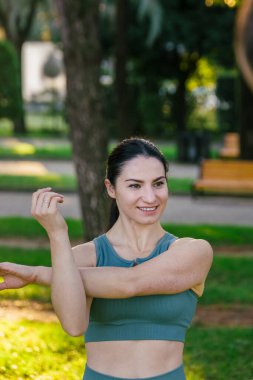 Sportif ve güler yüzlü genç bayan spor giyim koçu yeşil yaz parkında fiziksel esneme egzersizleri yapıyor. Spor açık hava konsepti.