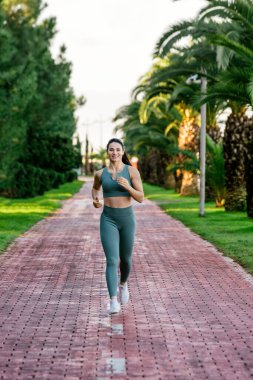 Sportif ve güler yüzlü genç bayan spor giyim koçu kırmızı koşu pistinde koşuyor. Spor açık hava konsepti.