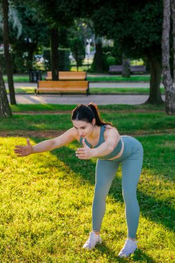 Sportif ve güler yüzlü genç bayan spor giyim koçu yeşil yaz parkında fiziksel esneme egzersizleri yapıyor. Spor açık hava konsepti.