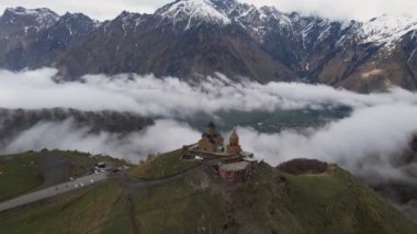 Gergeti Trinity Kilisesi 'nin, dağın üzerinden ağır sis bulutları akan hava aracı görüntüsü. Stepantsminda, Georgia yakınlarındaki karlı zirvelerin güzel dağ manzarası..