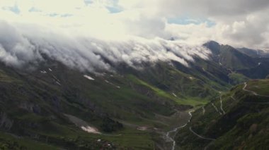 Yoğun sis bulutlarının dağın üzerinden uçuşunu gösteren hava aracı görüntüsü. Dağlarda asılı duran sisli bulutlar. Gürcistan, Gudauri yakınlarındaki karlı zirvelerin güzel dağ manzarası.