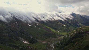 Yoğun sis bulutlarının dağın üzerinden uçuşunu gösteren hava aracı görüntüsü. Dağlarda asılı duran sisli bulutlar. Gürcistan, Gudauri yakınlarındaki karlı zirvelerin güzel dağ manzarası.