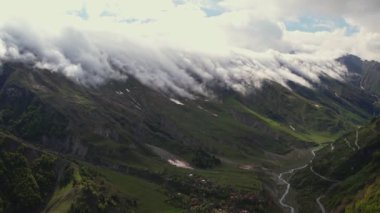 Yoğun sis bulutlarının dağın üzerinden uçuşunu gösteren hava aracı görüntüsü. Dağlarda asılı duran sisli bulutlar. Gürcistan, Gudauri yakınlarındaki karlı zirvelerin güzel dağ manzarası.