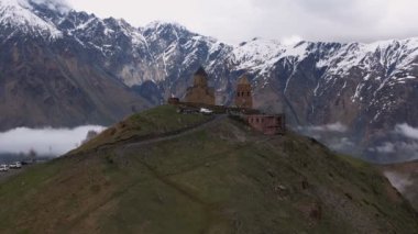 Gergeti Trinity Kilisesi 'nin, dağın üzerinden ağır sis bulutları akan hava aracı görüntüsü. Stepantsminda, Georgia yakınlarındaki karlı zirvelerin güzel dağ manzarası..