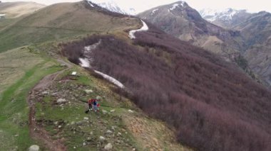 Gergeti Trinity Kilisesi 'nin yanındaki tepeden aşağı doğru koşan iki kadın dağın üzerinden ağır sis bulutları süzülüyor. Stepantsminda, Georgia yakınlarındaki karlı zirvelerin güzel dağ manzarası..