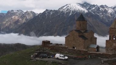 Gergeti Trinity Kilisesi 'nin, dağın üzerinden ağır sis bulutları akan hava aracı görüntüsü. Stepantsminda, Georgia yakınlarındaki karlı zirvelerin güzel dağ manzarası..