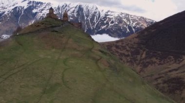Gergeti Trinity Kilisesi 'nin, dağın üzerinden ağır sis bulutları akan hava aracı görüntüsü. Stepantsminda, Georgia yakınlarındaki karlı zirvelerin güzel dağ manzarası..