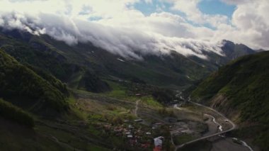 Yoğun sis bulutlarının dağın üzerinden uçuşunu gösteren hava aracı görüntüsü. Dağlarda asılı duran sisli bulutlar. Gürcistan, Gudauri yakınlarındaki karlı zirvelerin güzel dağ manzarası.