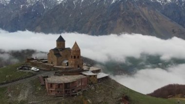 Gergeti Trinity Kilisesi 'nin, dağın üzerinden ağır sis bulutları akan hava aracı görüntüsü. Stepantsminda, Georgia yakınlarındaki karlı zirvelerin güzel dağ manzarası..