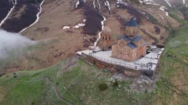 Gergeti Trinity Kilisesi 'nin, dağın üzerinden ağır sis bulutları akan hava aracı görüntüsü. Stepantsminda, Georgia yakınlarındaki karlı zirvelerin güzel dağ manzarası..