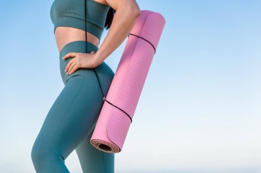 Spor ve spor salonu, spor giyim bölümünde elinde yoga minderiyle tanınmayan genç spor atletik bayan fitness koçunun kapısına yakın. Spor açık hava konsepti.