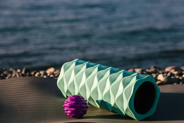 Yuvarlak fitness topu denizin kenarındaki yoga minderinde yatıyor. Spor açık hava konsepti.