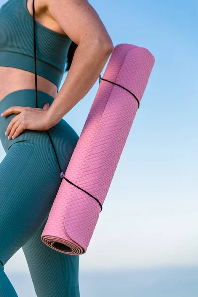 Spor ve spor salonu, spor giyim bölümünde elinde yoga minderiyle tanınmayan genç spor atletik bayan fitness koçunun kapısına yakın. Spor açık hava konsepti.