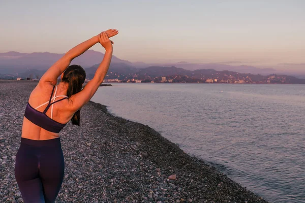 Spor ve spor açık hava konsepti. Sportif ve gülen atletik spor salonu antrenörü spor kıyafeti giyiyor plajda yoga egzersizleri yapıyor..