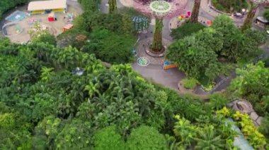 Bulut Ormanı ve Çiçek Kubbesi 'nin havadan görünüşü alacakaranlıkta aydınlandı. Arka planda ünlü bir otel. Körfez kenarındaki bahçeler, Singapur şehri 4K.