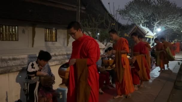伝統的な神聖な施しの儀式で施しのボウルを持つ僧侶 地元の人々や観光客は ラオスのルアンパバーンにある仏教の僧侶のボウルに食べ物を入れました ラオスのビエンチャン 2023年3月4日 — ストック動画