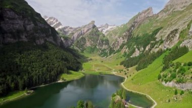 Aerial view of a mountainous landscape in Seealpsee, Switzerland. Drone footage of rocky Schafler Mountain and Seealpsee Lake under bright sunlight.