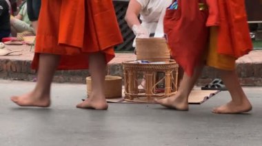 Rahiplerin ayakları geleneksel kutsal sadaka verme töreninde. Yerel halk ve turistler, Luang Prabang, Laos 'taki Budist rahiplerin kaselerine yemek sundular. Luang Prabang, Laos - 03 Mart 2023. 