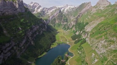 Aerial view of a mountainous landscape in Seealpsee, Switzerland. Drone footage of rocky Schafler Mountain and Seealpsee Lake under bright sunlight.