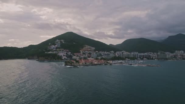 モンテネグロのアドリア海で美しい夏の朝に日没するバドヴァ市近くの美しいスヴェティーニャ島の空中ドローンビュー — ストック動画
