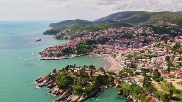夏季にはモンテネグロの美しい都市ウルシンジの上空を飛行するドローン 古い都市の石造りの家とアドリア海のビーチで泳ぐ人々 — ストック動画