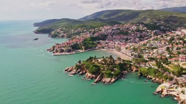 夏季にはモンテネグロの美しい都市ウルシンジの上空を飛行するドローン 古い都市の石造りの家とアドリア海のビーチで泳ぐ人々 — ストック動画